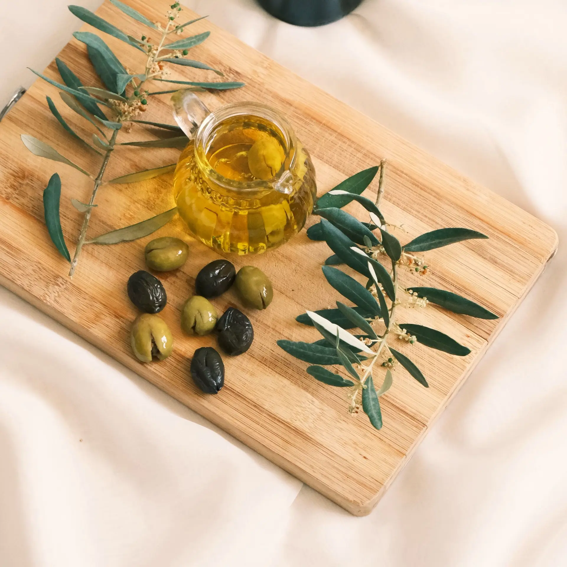 Tabla de madera con aceitunas, ramas de olivo y una jarra de aceite